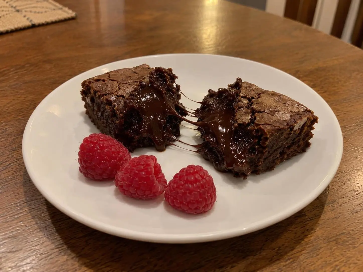 AI-made sample phone photo of a chocolate lava brownie in two halves with a molten pull and three raspberries; generated demonstration, not a real customer dish.