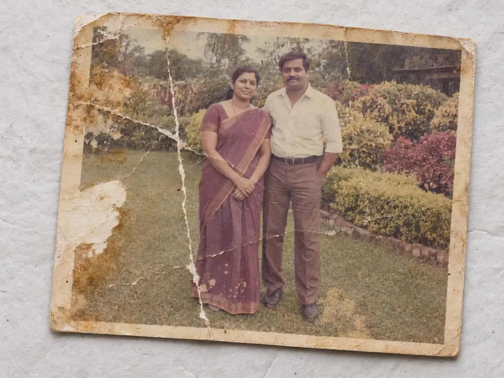 A torn, creased print of a couple standing in a garden, before AI restoration.
